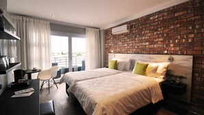 Habitación de hotel con dos camas, un escritorio, una silla y un amplio ventanal con cortinas.