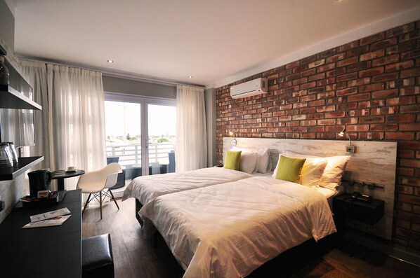 Habitación de hotel con dos camas, un escritorio, una silla y un amplio ventanal con cortinas.