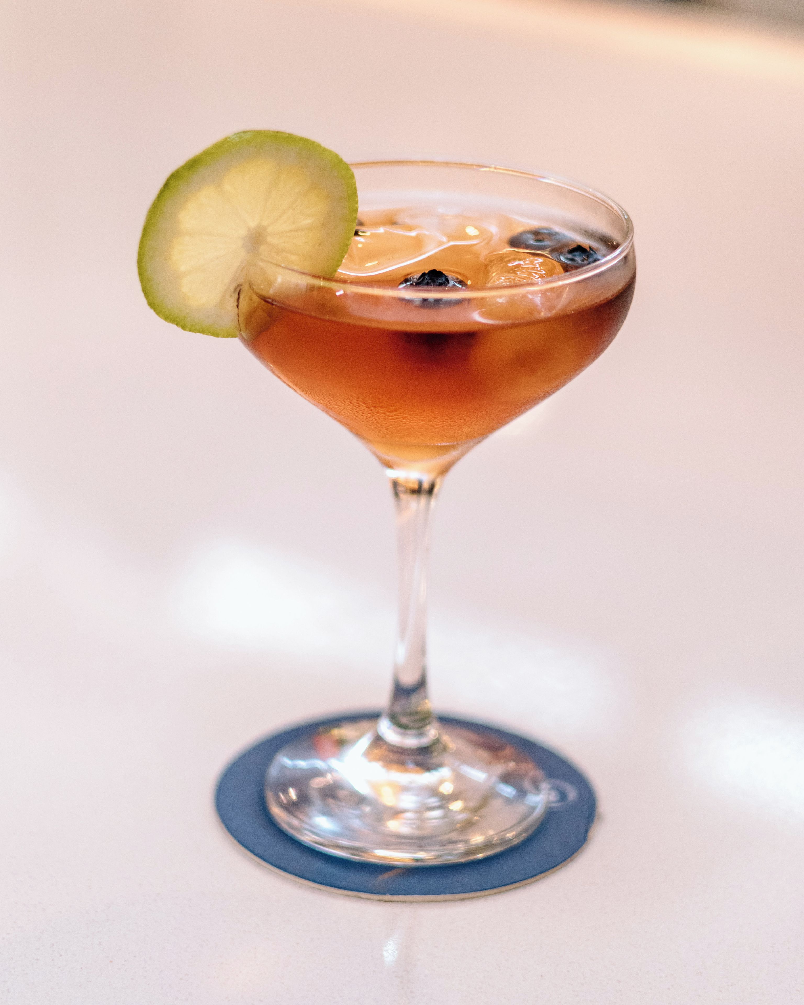 Een cocktailglas met een limoenpartje op een blauwe onderzetter.