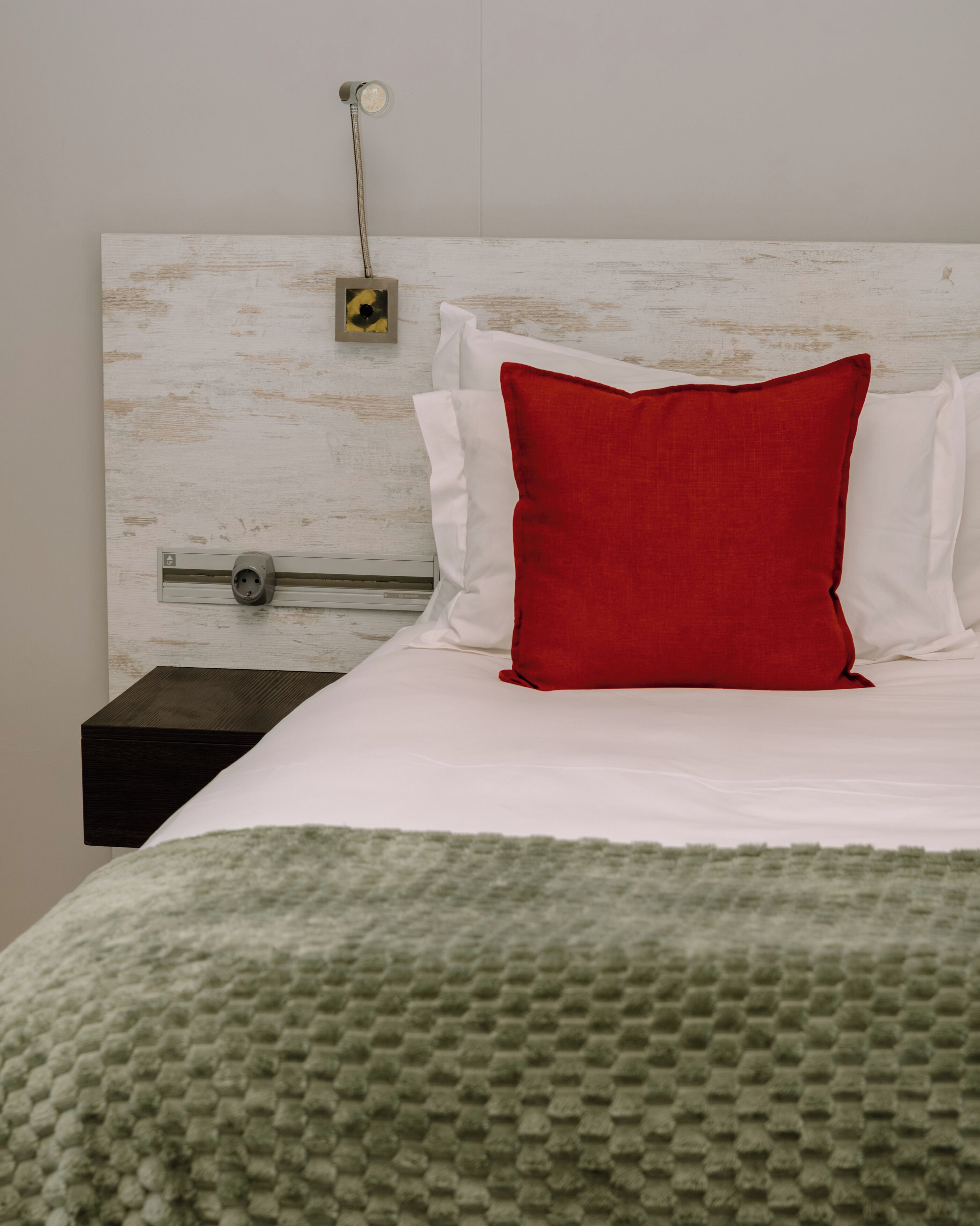 Ein Bett mit weißen und roten Kissen, ein Nachttisch und eine Wand-Klimaanlage.