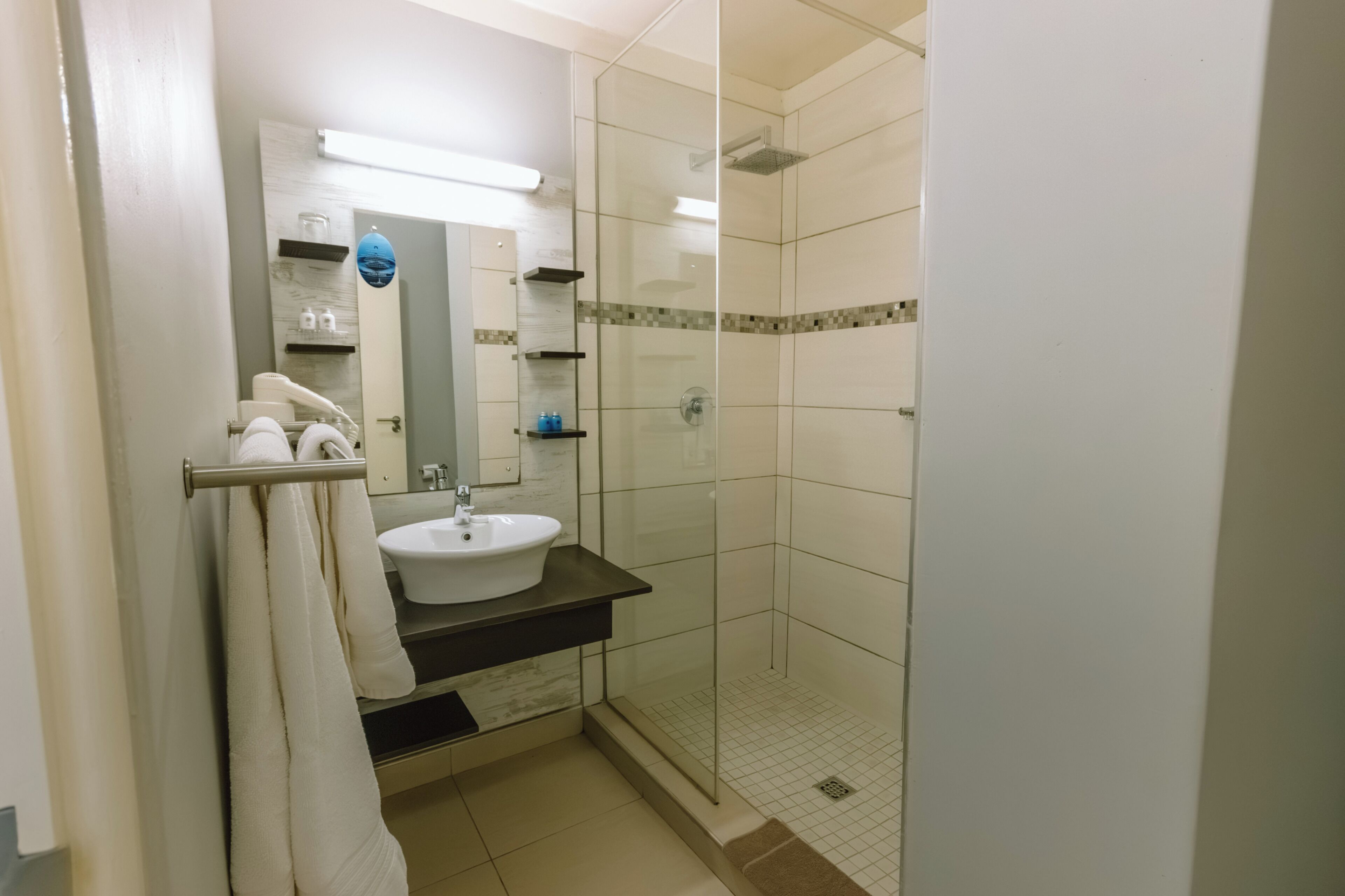 Un baño con lavamanos blanco, cabina de ducha con mampara de vidrio y perchero.