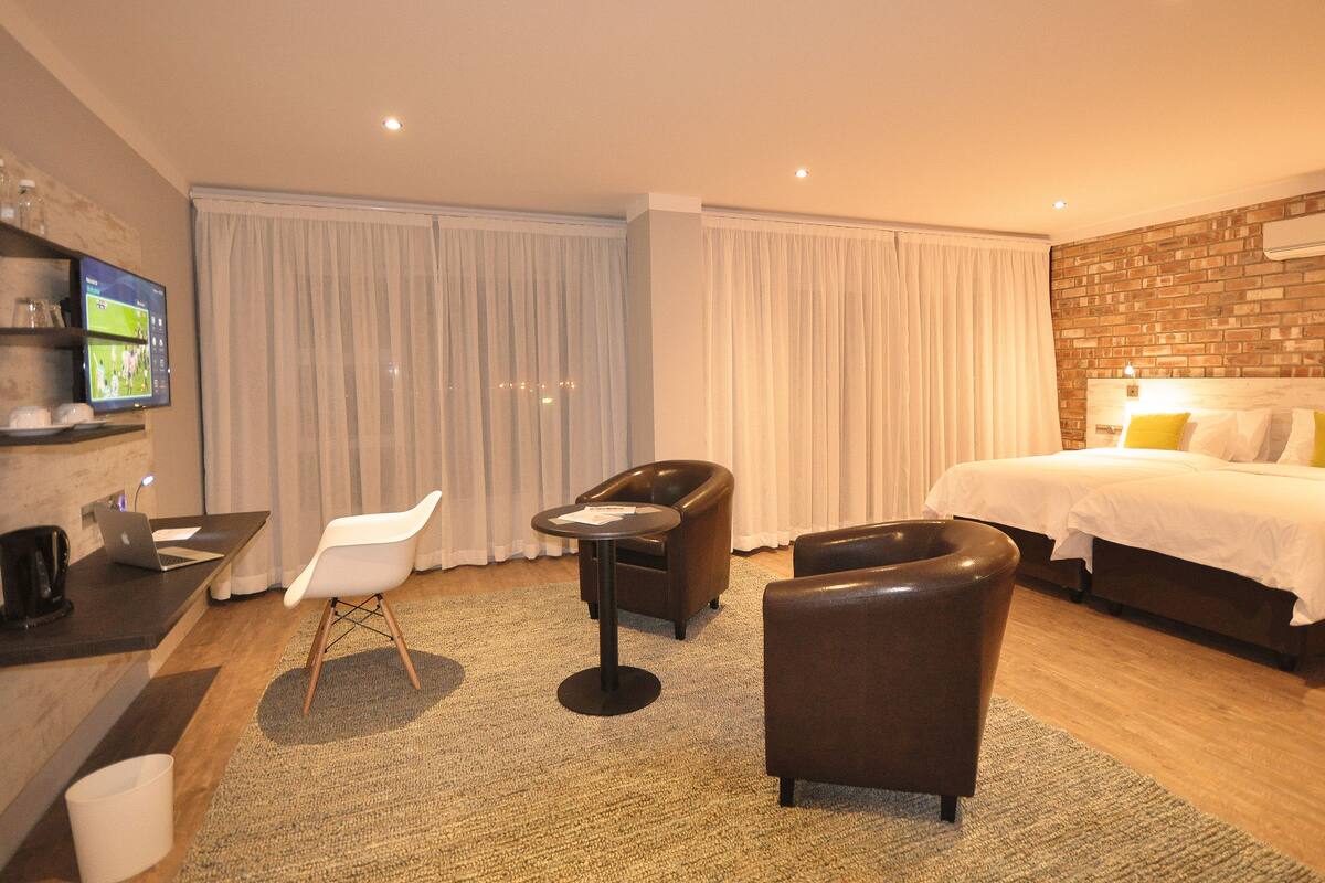 A hotel room with a bed, a desk with a laptop, a TV, and a seating area with chairs.