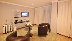 A modern hotel room with a flat-screen TV, a coffee maker, a laptop, a sofa, and two chairs.