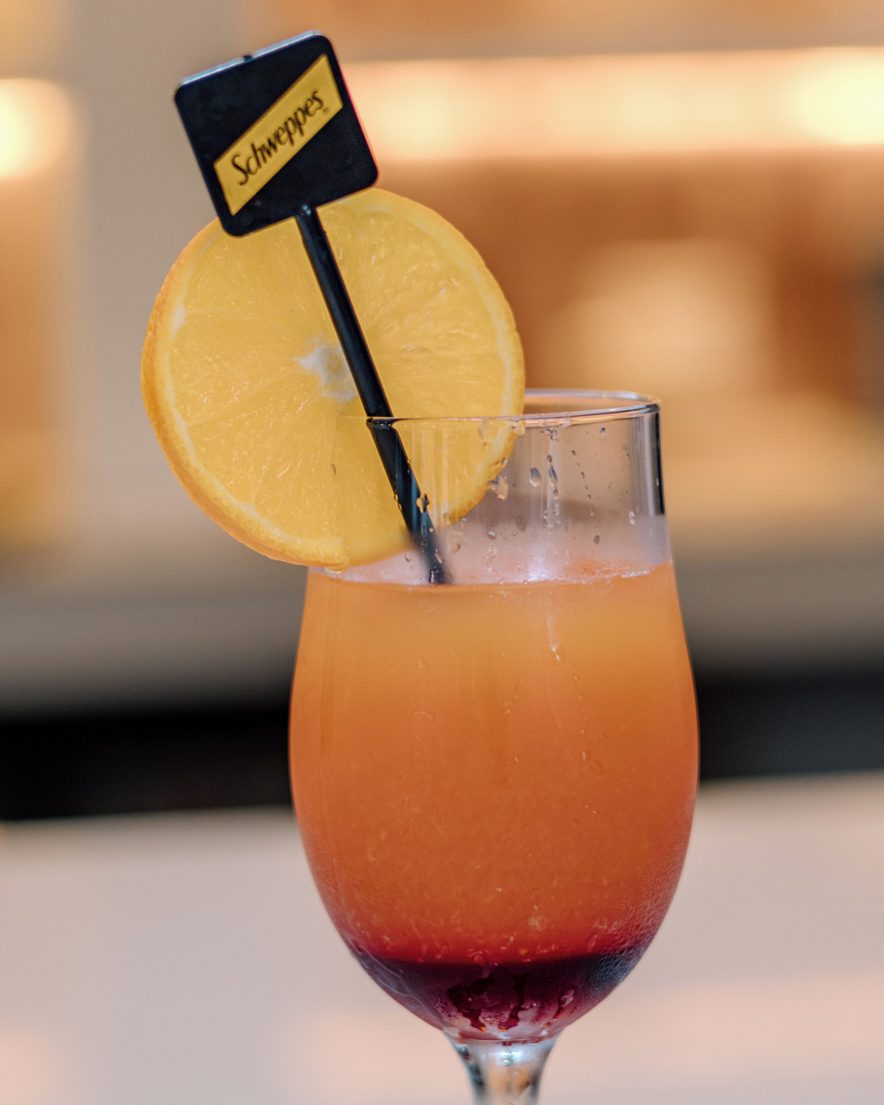 Un vaso con una bebida en capas, una rodaja de naranja y una etiqueta.