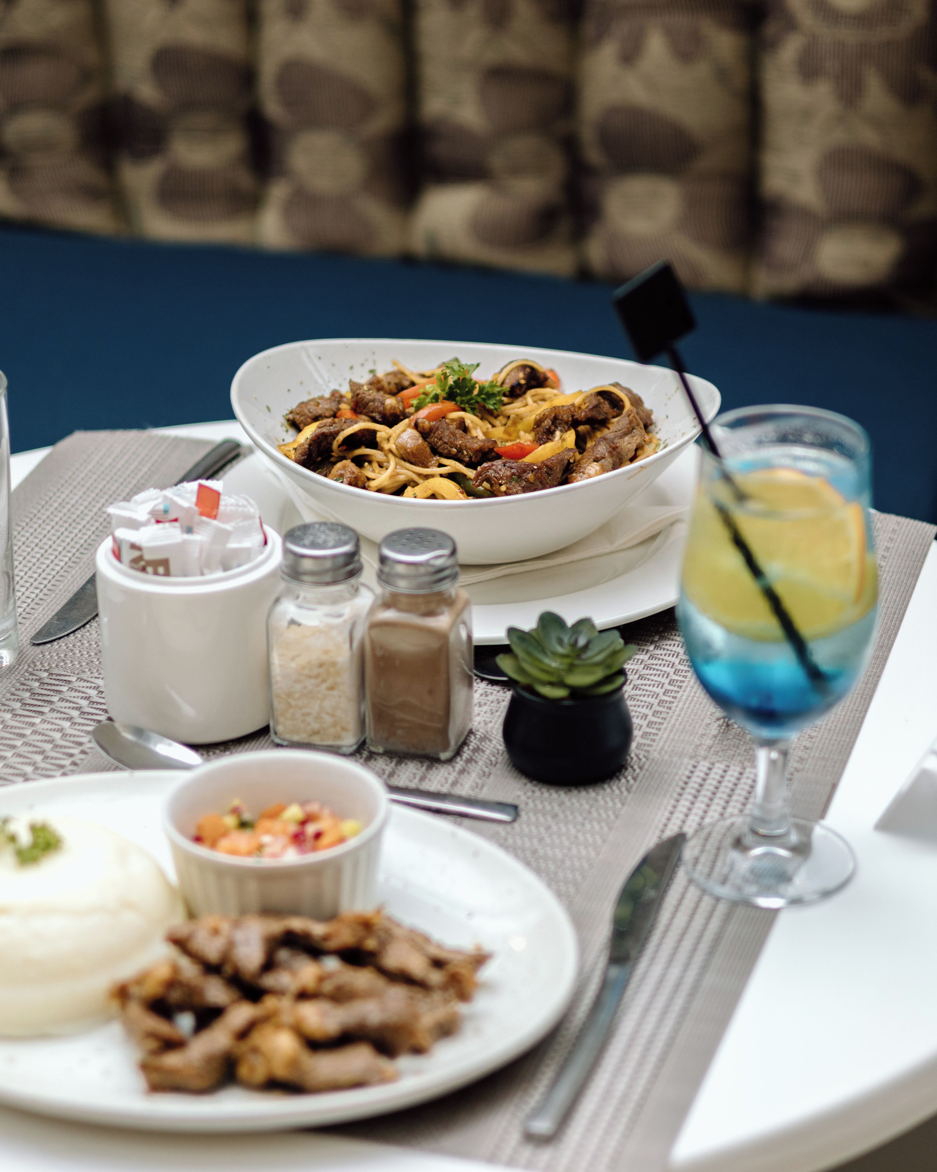 A dining table with a bowl of food, a glass of drink, condiments, and a small plant.
