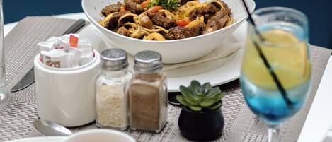 A dining table with a bowl of food, a glass of drink, condiments, and a small plant.