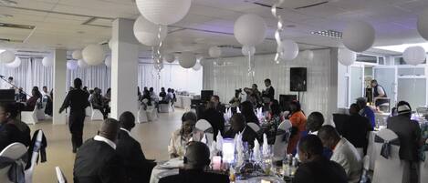 A banquet hall with round tables, white chairs, and hanging paper lanterns.