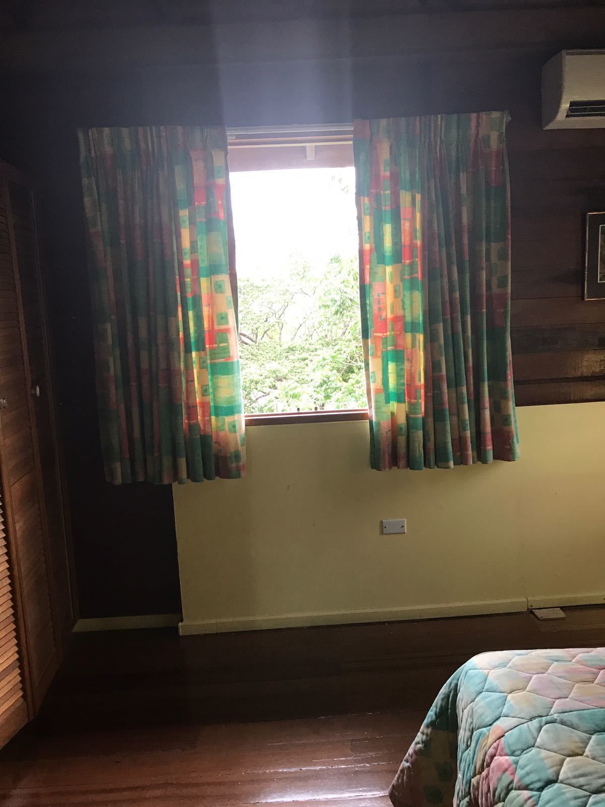 A room with a window covered by colorful curtains, a wooden floor, and a bed with a quilt.