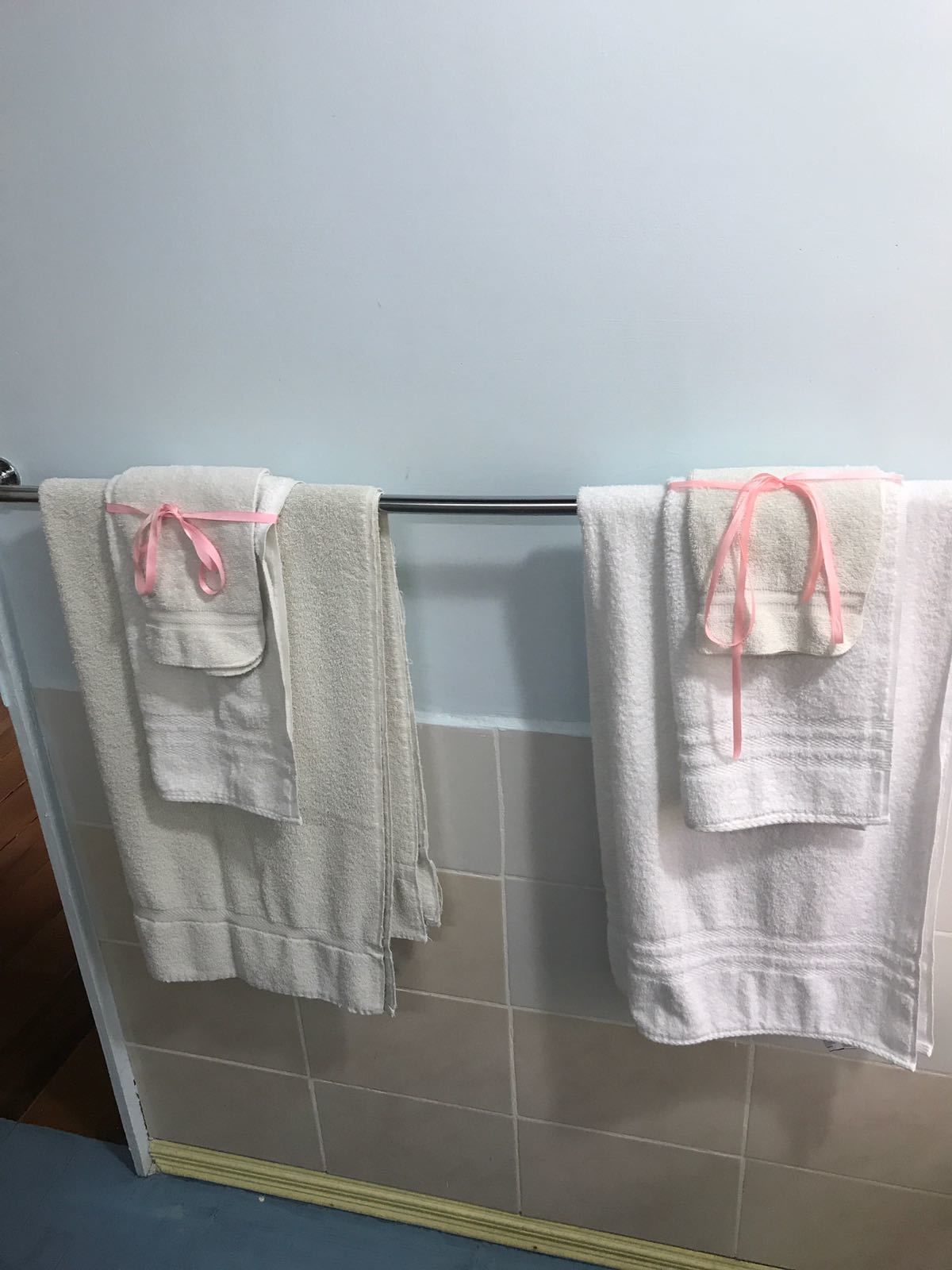 Um banheiro com duas toalhas brancas penduradas em um porta-toalhas de metal, amarradas com fitas cor-de-rosa.