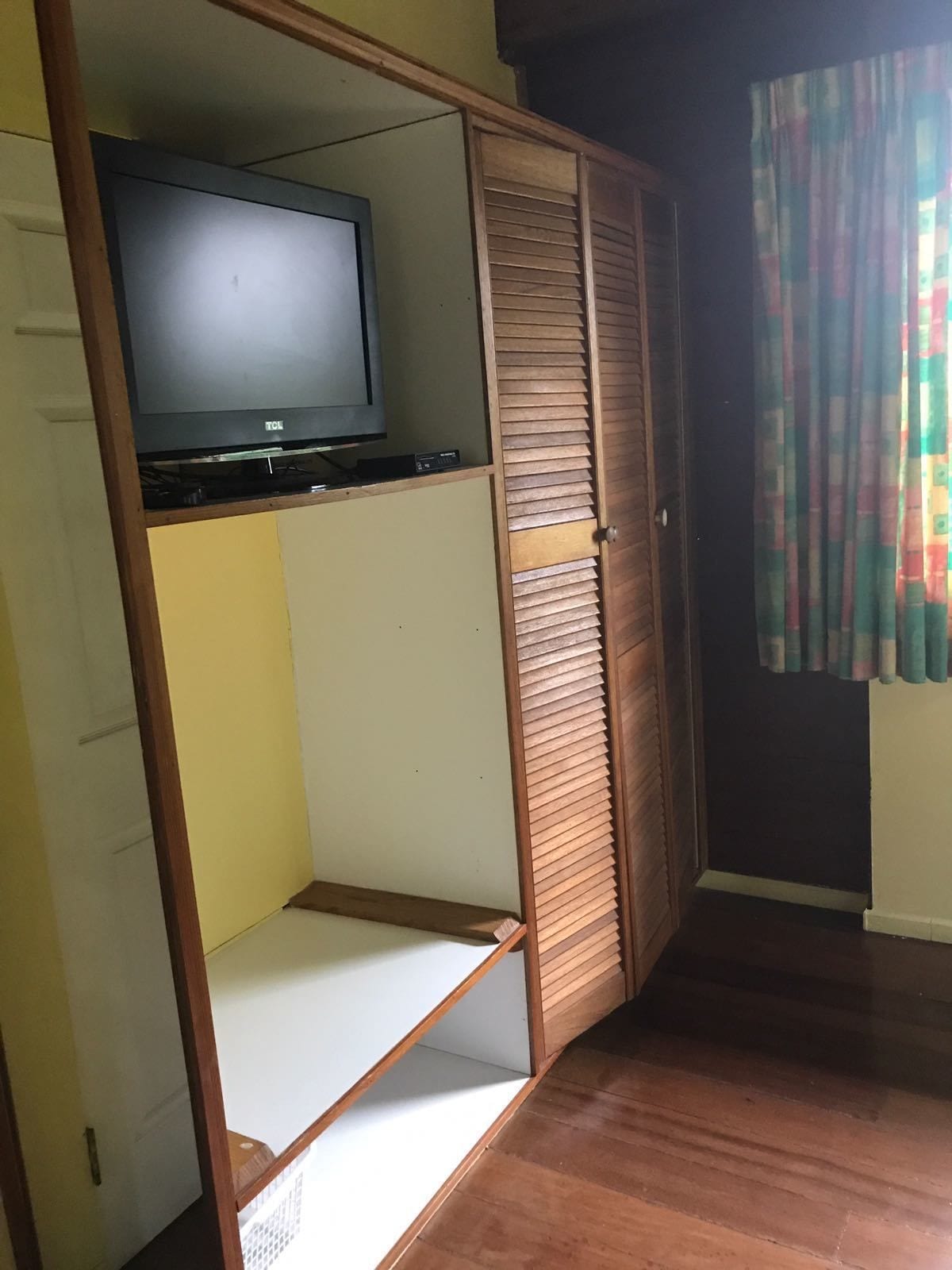 Una habitación con un armario de madera, un televisor encima y una cortina colorida.