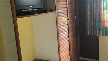 Una habitación con un armario de madera, un televisor encima y una cortina colorida.