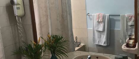 A bathroom with a large mirror, a sink, a hairdryer, a plant, and towels on a rack.