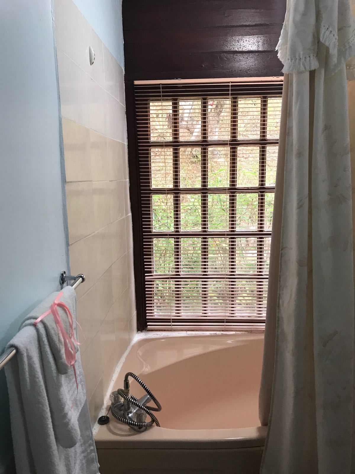 A bathroom with a bathtub, a window with blinds, and a towel rack with a towel.