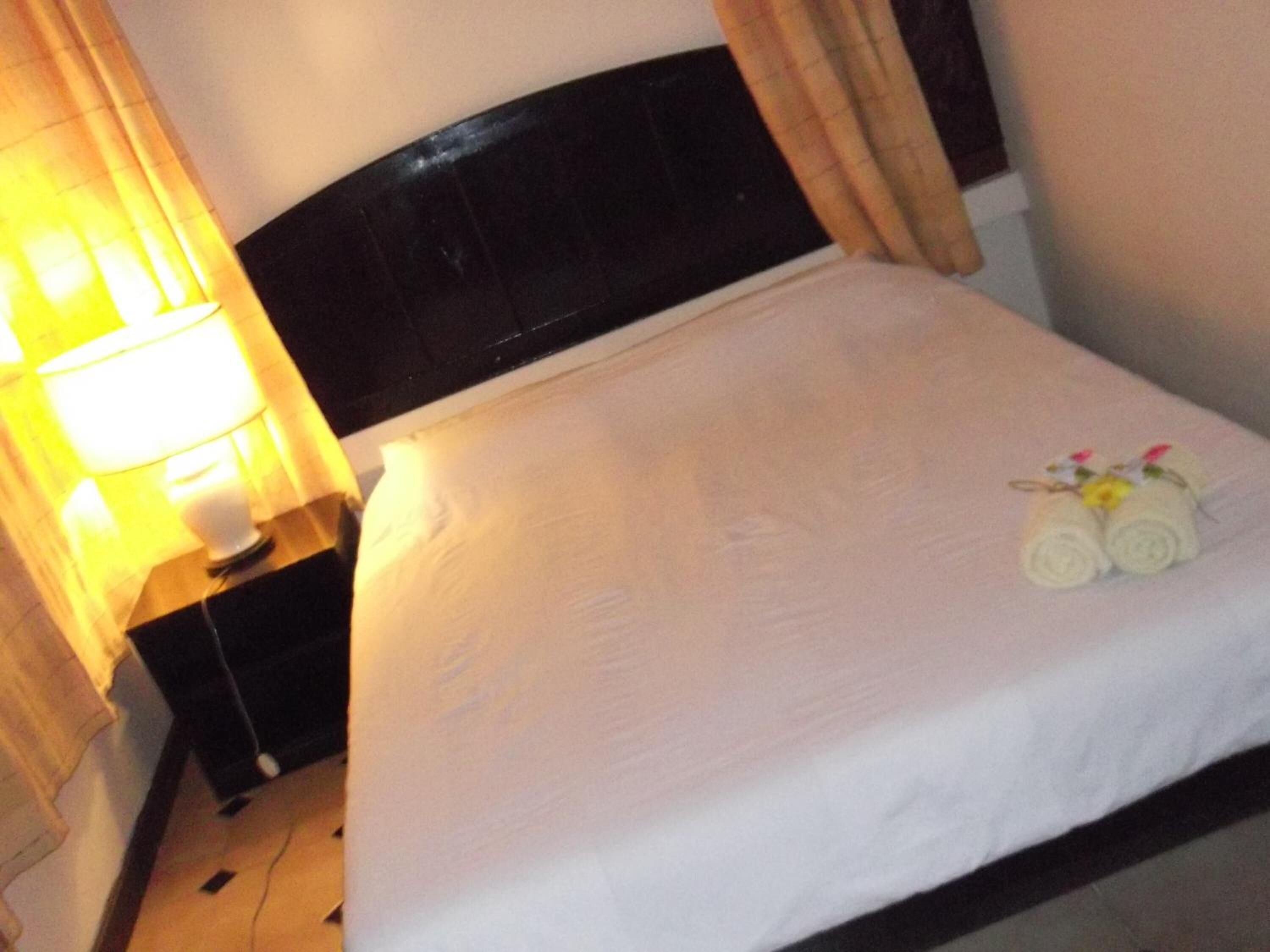 A neatly made bed with a white duvet, a dark headboard, and a lamp on a bedside table.