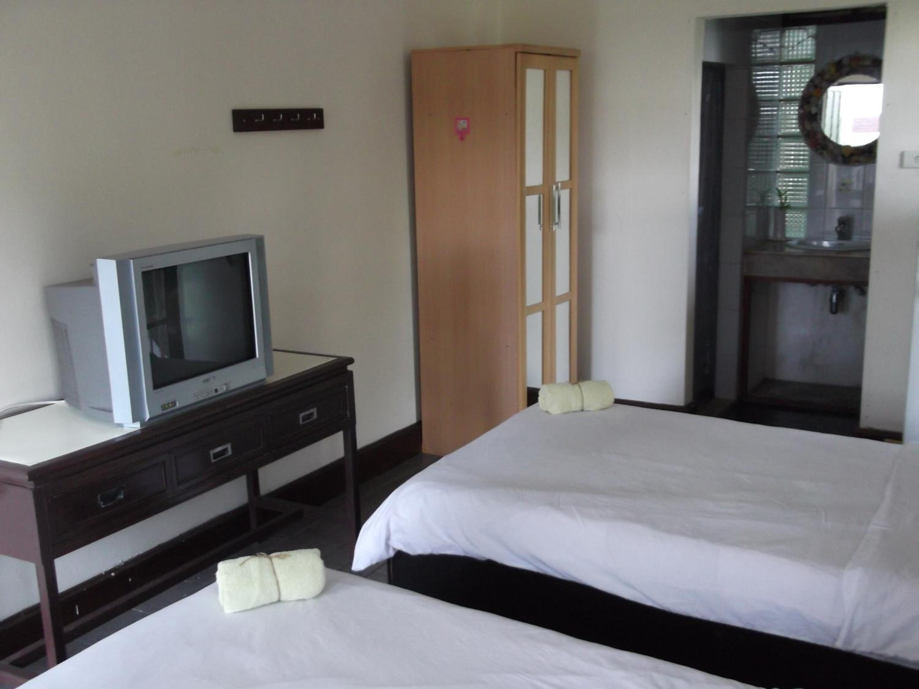 A hotel room with two beds, a television on a desk, a wardrobe, and a bathroom visible through an open door.