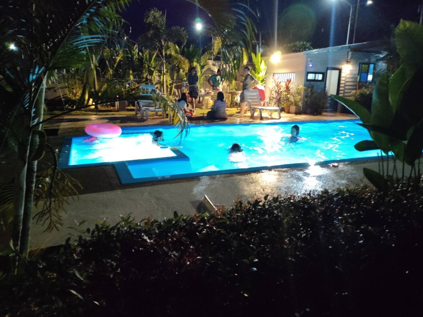 Une piscine illuminée la nuit, avec des gens qui nagent et qui sont assis autour.