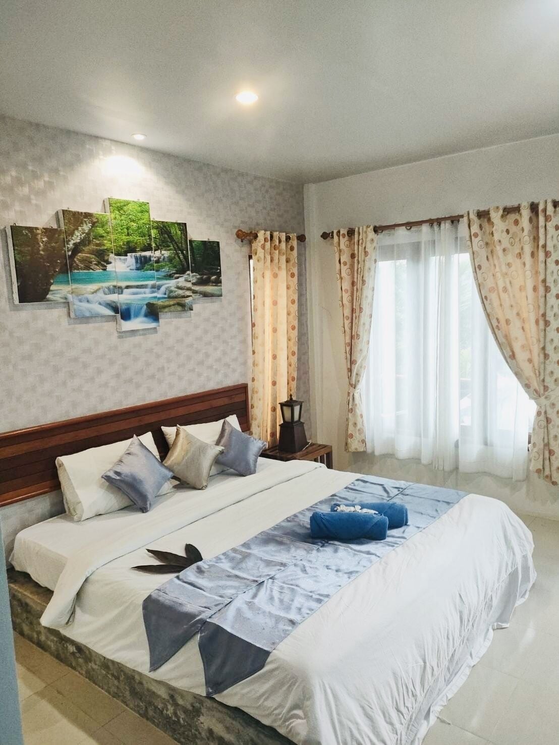 A hotel room with a large bed, a nightstand, a wall-mounted lamp, and a window with curtains.