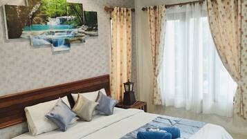 A hotel room with a large bed, a nightstand, a wall-mounted lamp, and a window with curtains.