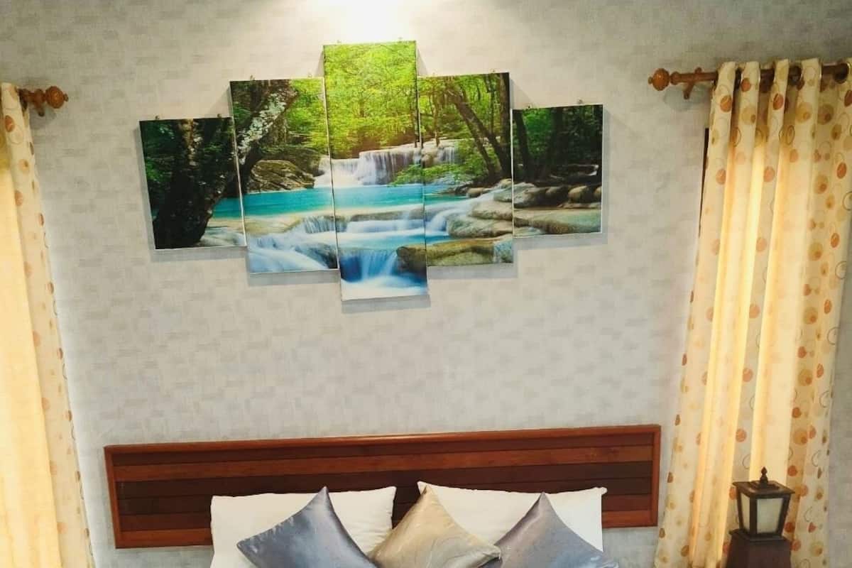 A neatly made bed with a blue and white bedspread, a set of blue towels with flowers, and a wall-mounted painting of a waterfall.