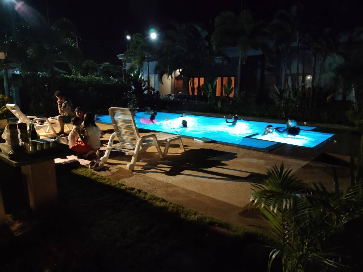 Un espace extérieur avec piscine, ouvert la nuit, comprenant des chaises longues et un bar.