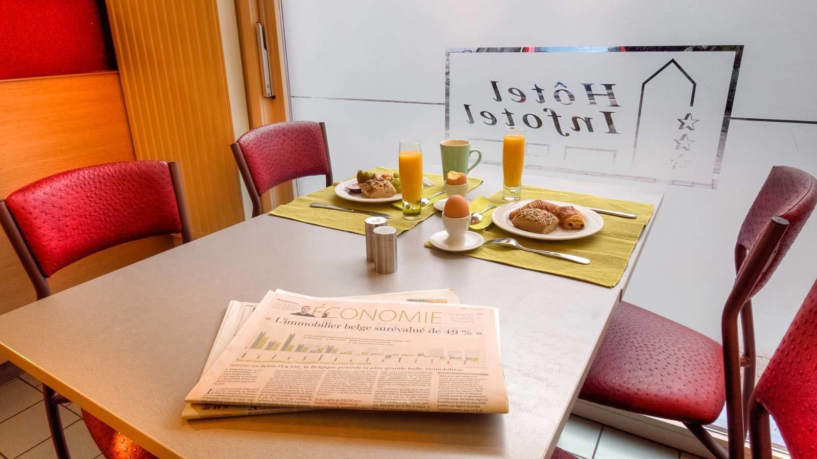 Une table de petit-déjeuner dressée avec un journal, du jus d’orange, du café et des viennoiseries.