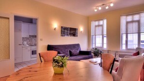 A modern living room with a wooden dining table, purple sofa, and striped chairs. - Hotel Infotel (Mons)