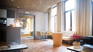A modern hotel lobby with a wooden parquet floor, a seating area with a sofa and chairs, a reception desk, and large windows with curtains. - Hotel d'Alcantara (Tournai)