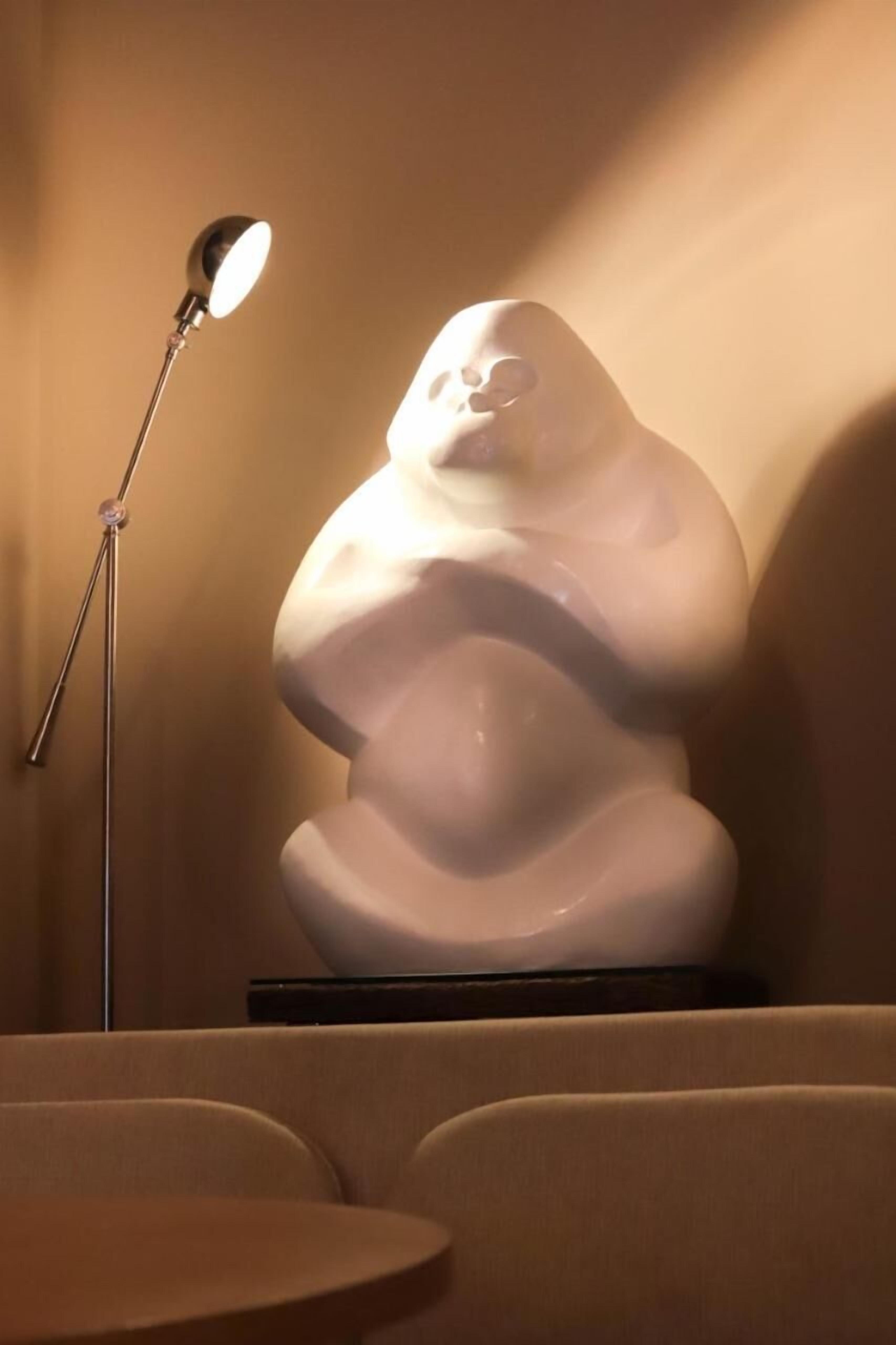 A sculpture of a human figure in a modern setting with a floor lamp to the left.