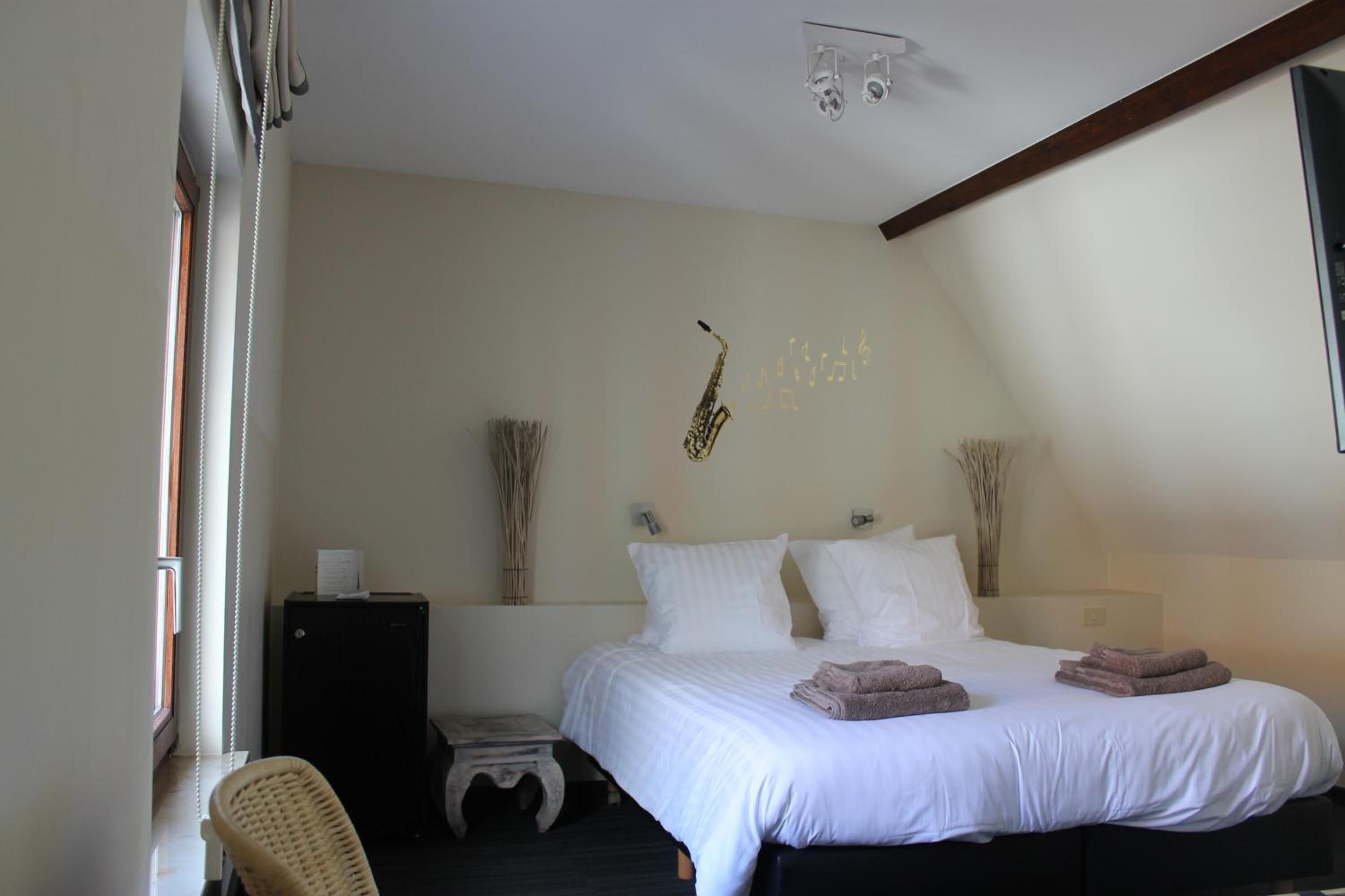 Un dormitorio con cama, una silla, una mesita y una lámpara de pared.