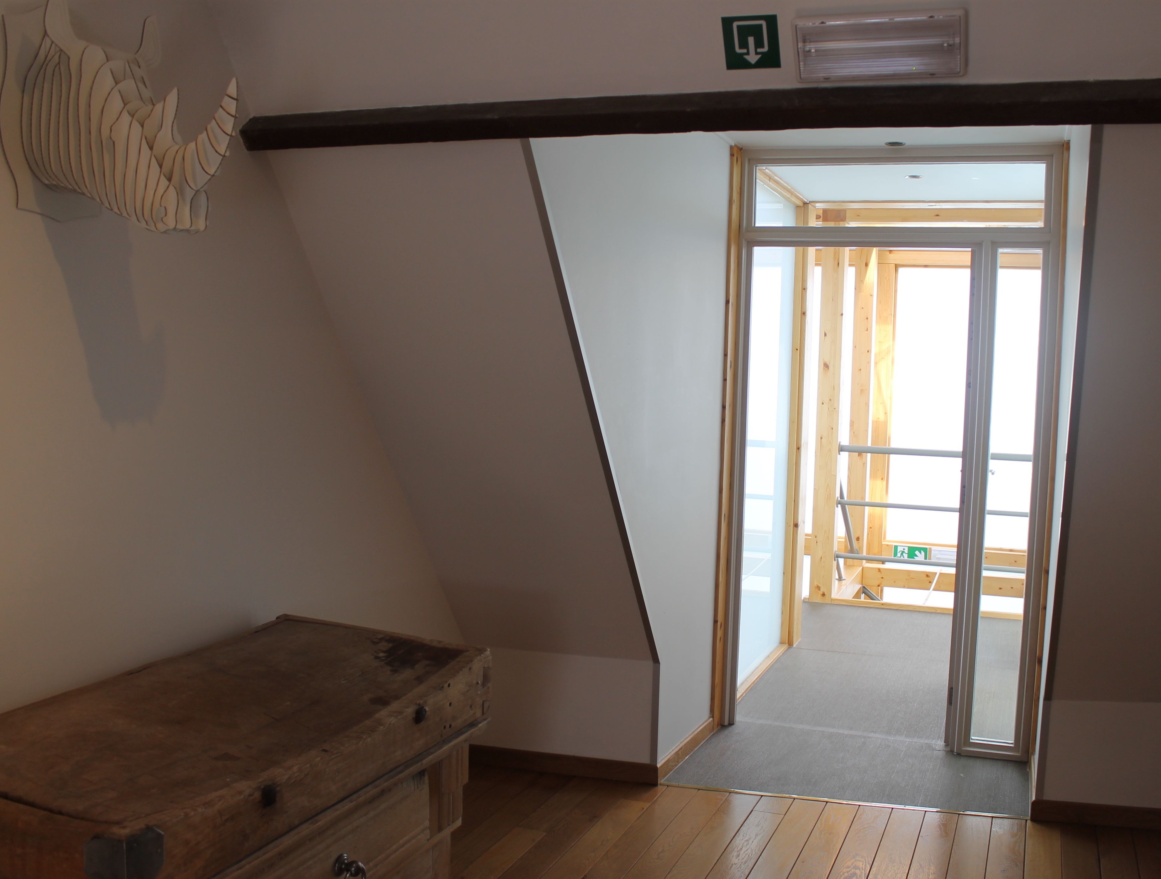A room with a sloped ceiling, a wooden bench, a door leading to an outdoor area, and a small staircase.