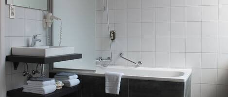 Un baño moderno con un lavamanos blanco, baldosas oscuras, una bañera grande y un espejo sobre el lavamanos.