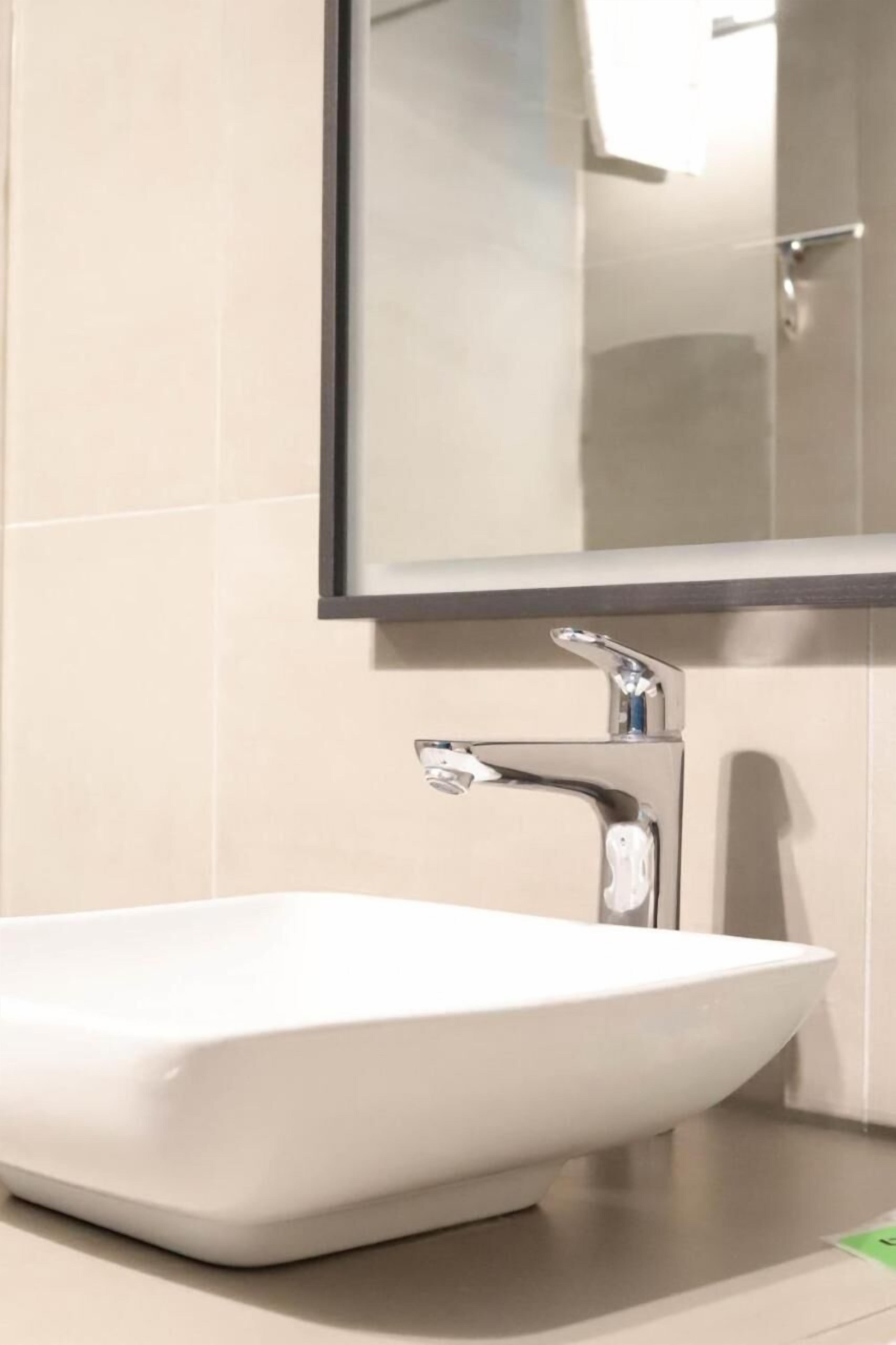 Une salle de bain avec un lavabo sur colonne blanc, un robinet chromé et un miroir au-dessus du lavabo.