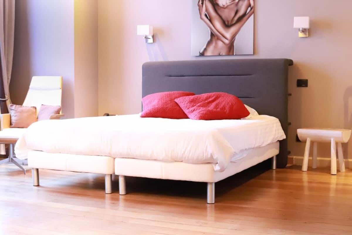 A modern bedroom with a large bed, two bedside tables, a chair, and a wall-mounted artwork.