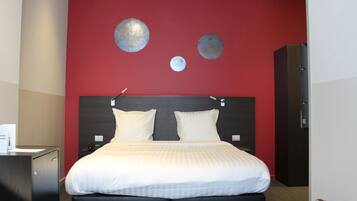 Quarto de hotel com uma cama grande, duas almofadas, cabeceira e parede de destaque vermelha com decorações circulares.