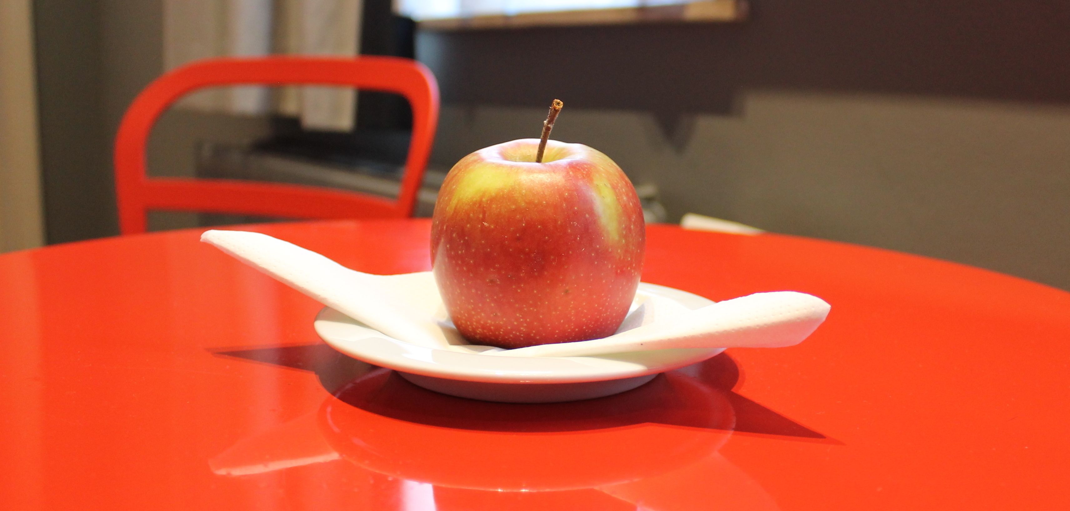 Una manzana sobre un plato blanco con una cuchara en una mesa roja.