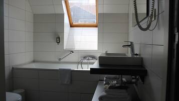 A bathroom with a skylight, a bathtub, a toilet, and a sink.