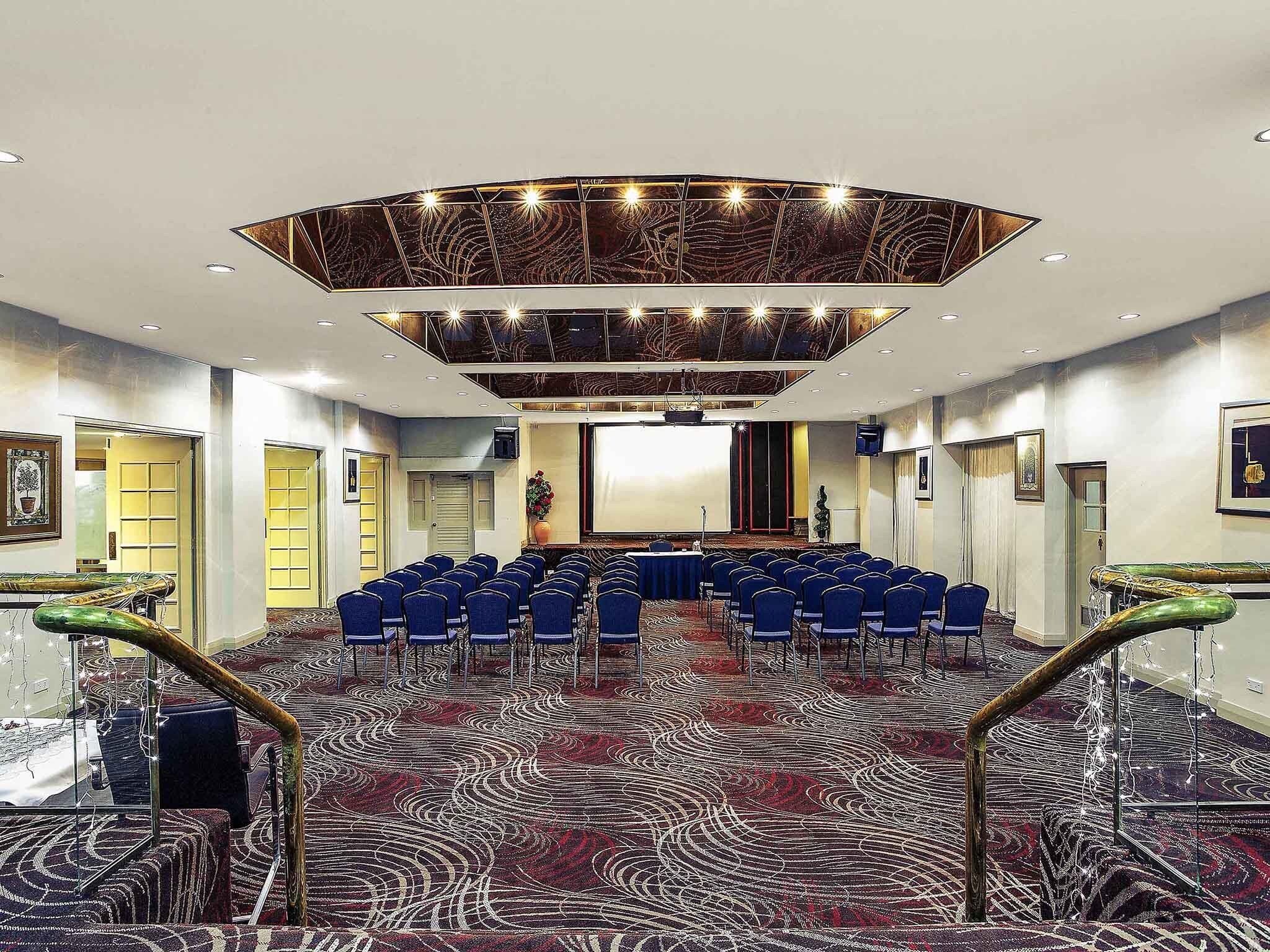 A conference room with a patterned carpet, blue chairs, a stage, and a modern ceiling design.