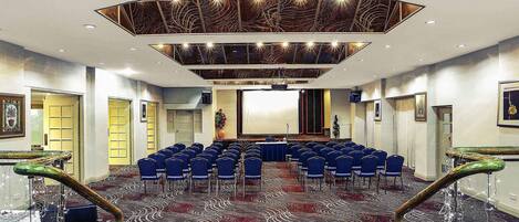 A conference room with a patterned carpet, blue chairs, a stage, and a modern ceiling design.