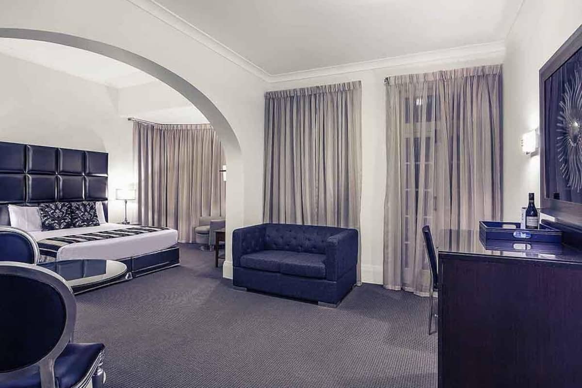 A hotel room with a bed, a sofa, a desk, and a chair.