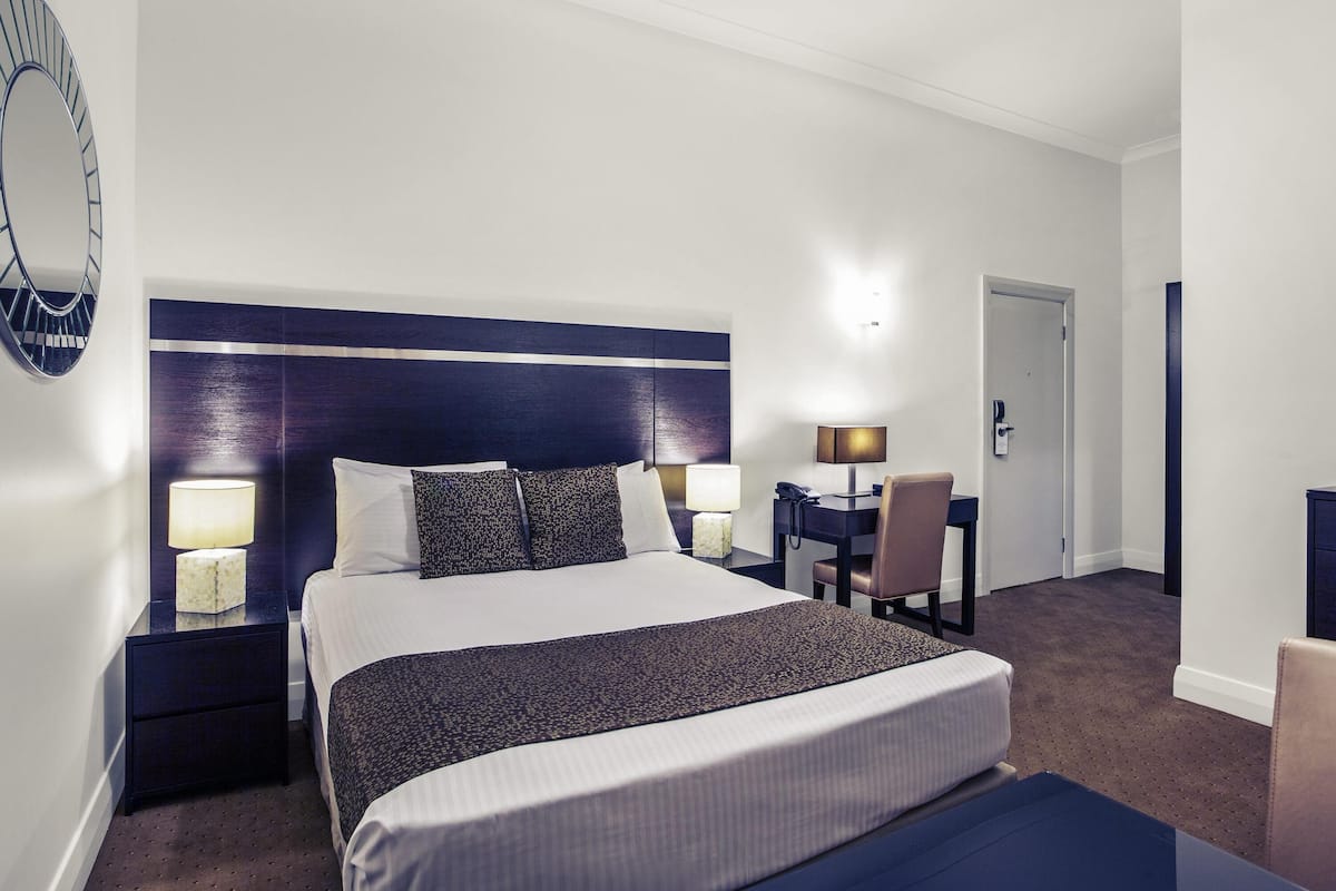 Una habitación de hotel con una cama grande, lámparas de noche, un escritorio con una silla y una puerta.