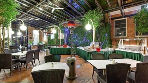 An outdoor dining area with tables and chairs, a central heating lamp, and a brick wall with greenery. - Mercure Maitland Monte Pio (Maitland)