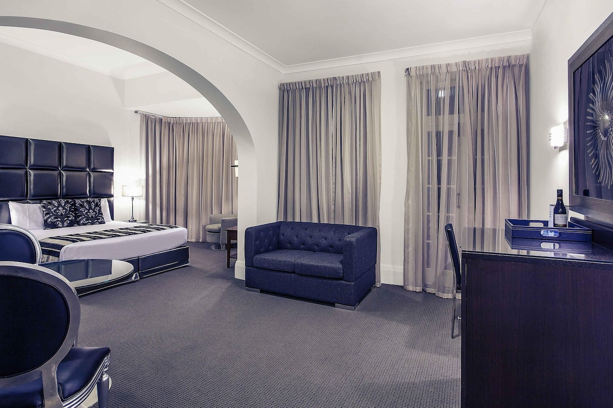 A hotel room with a bed, a seating area, a desk, and a large mirror.
