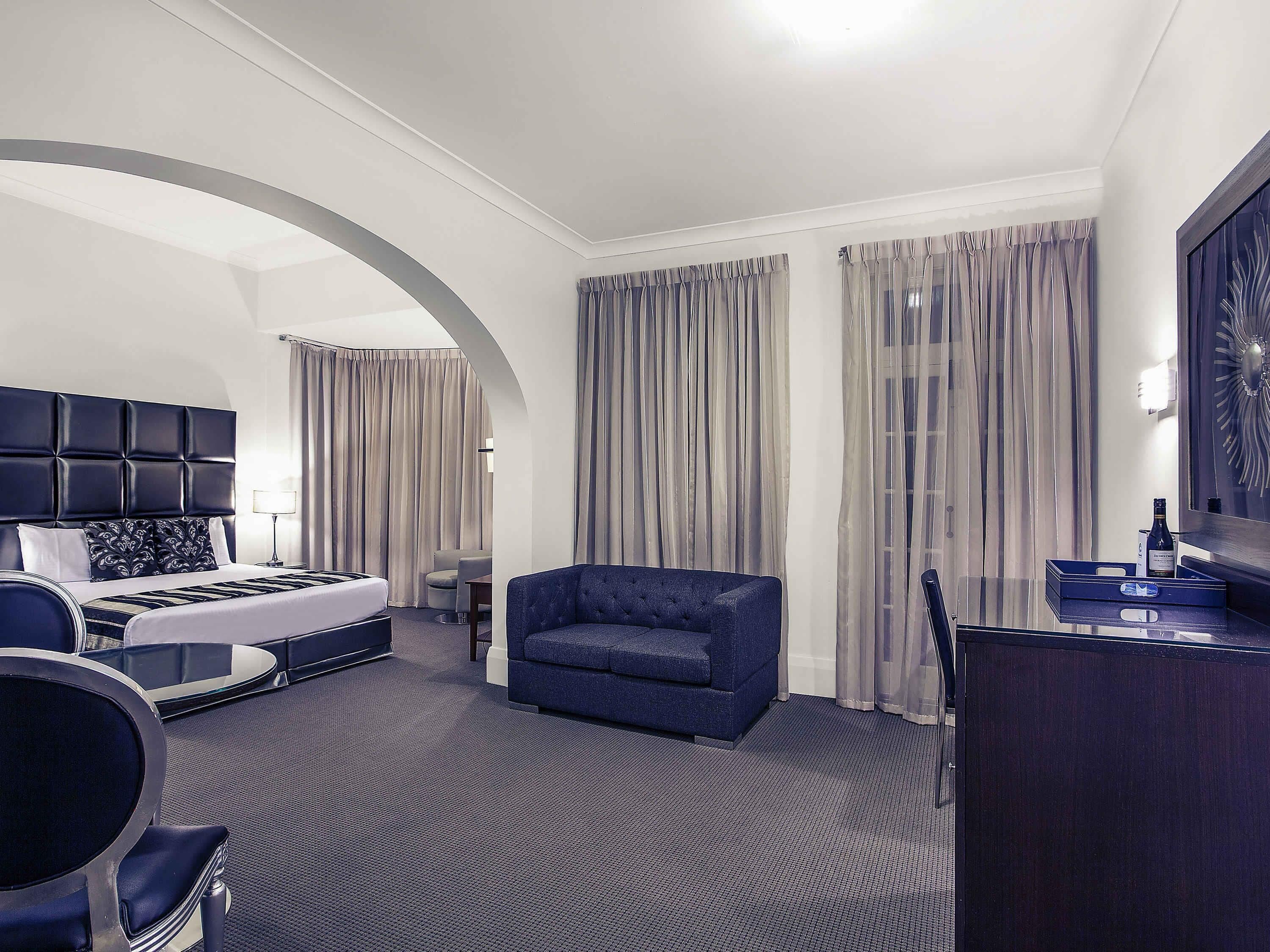 Une chambre d’hôtel comprenant un lit, un coin salon, un bureau et un grand miroir.