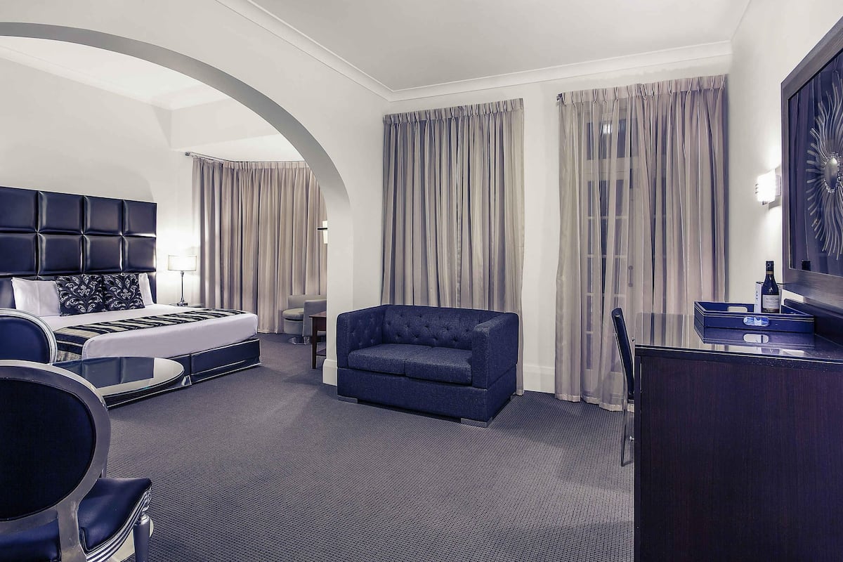 A hotel room with a bed, a seating area, a desk, and a large mirror.