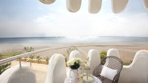 Un balcone con vista sulla spiaggia, una sedia in vimini, un tavolino con un vaso di fiori e una bottiglia di crema solare.