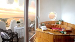 Un balcone con vista sul mare, una vasca da bagno in legno con petali di rosa e un tavolo bianco con fiori e una gabbia per uccelli.