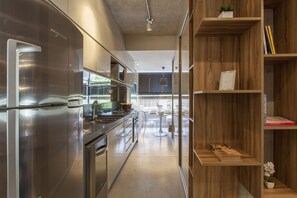 Een moderne keuken met roestvrijstalen apparatuur, een eethoek met een witte tafel en stoelen, en houten planken met boeken en een kleine plant.