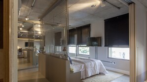 Quarto moderno com uma cama grande, divisória de vidro e TV fixada na parede.