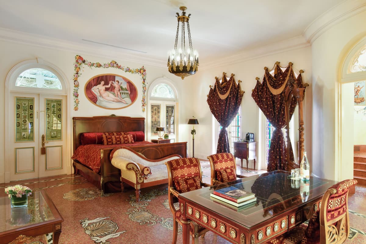 Una habitación con una cama grande, una mesa de vidrio, sillas ornamentadas y un candelabro.