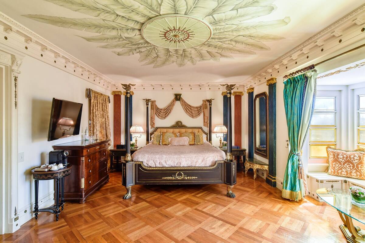 Un dormitorio lujoso con una cama grande, techo ornamentado y decoración clásica.